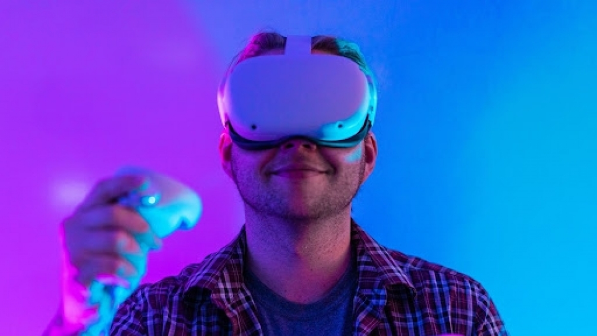 Person using a VR headset and controller in an immersive learning environment illuminated with colorful lighting.